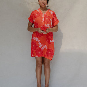 woman with brown hair wearing a retro orange v neck dress with flower pattern
