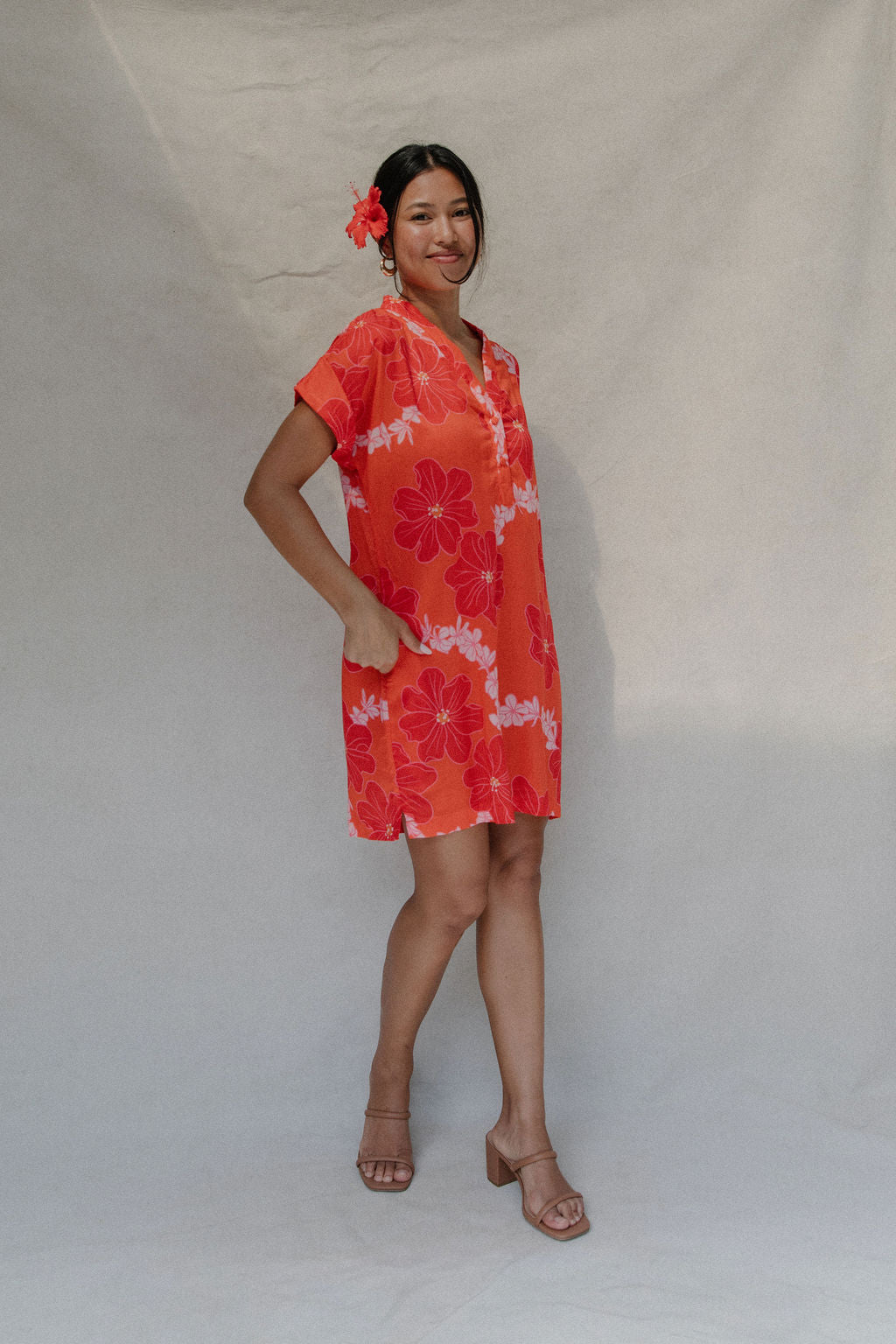 woman with brown hair wearing a retro orange v neck dress with flower pattern