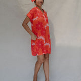 woman with brown hair wearing a retro orange v neck dress with flower pattern