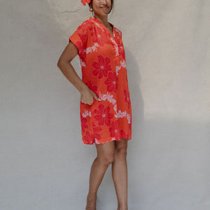 woman with brown hair wearing a retro orange v neck dress with flower pattern