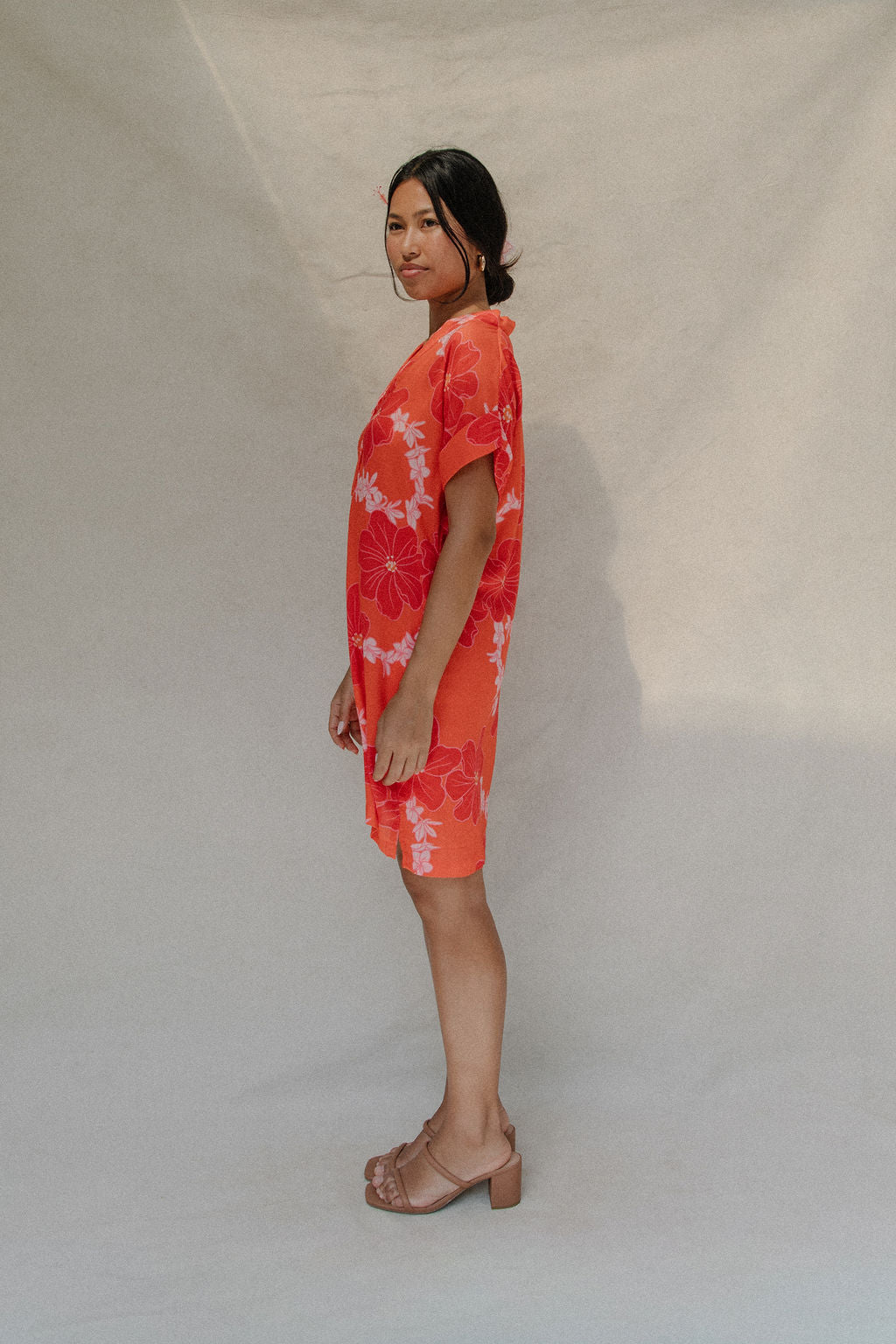 woman with brown hair wearing a retro orange v neck dress with flower pattern