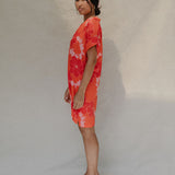 woman with brown hair wearing a retro orange v neck dress with flower pattern