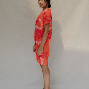 woman with brown hair wearing a retro orange v neck dress with flower pattern