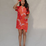 woman with brown hair wearing a retro orange v neck dress with flower pattern