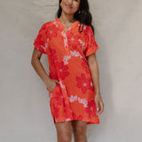 woman with brown hair wearing a retro orange v neck dress with flower pattern