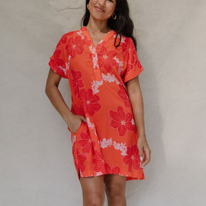 woman with brown hair wearing a retro orange v neck dress with flower pattern