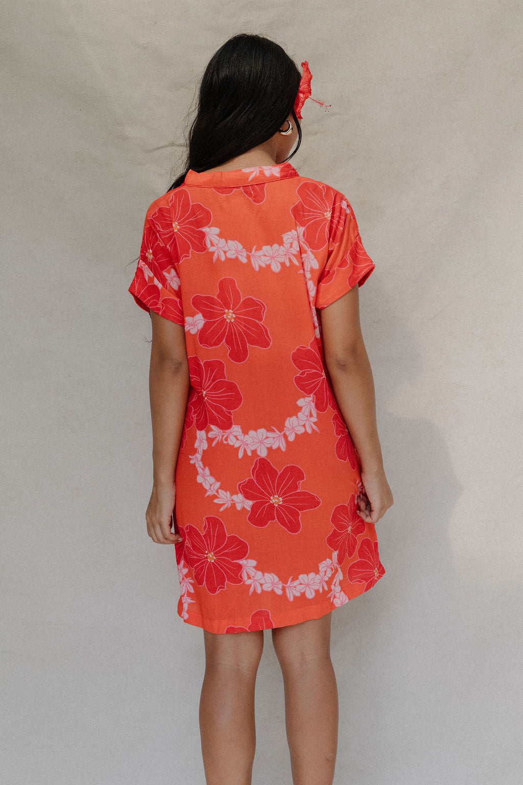 woman with brown hair wearing a retro orange v neck dress with flower pattern
