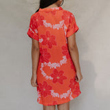 woman with brown hair wearing a retro orange v neck dress with flower pattern