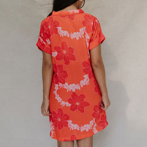 woman with brown hair wearing a retro orange v neck dress with flower pattern
