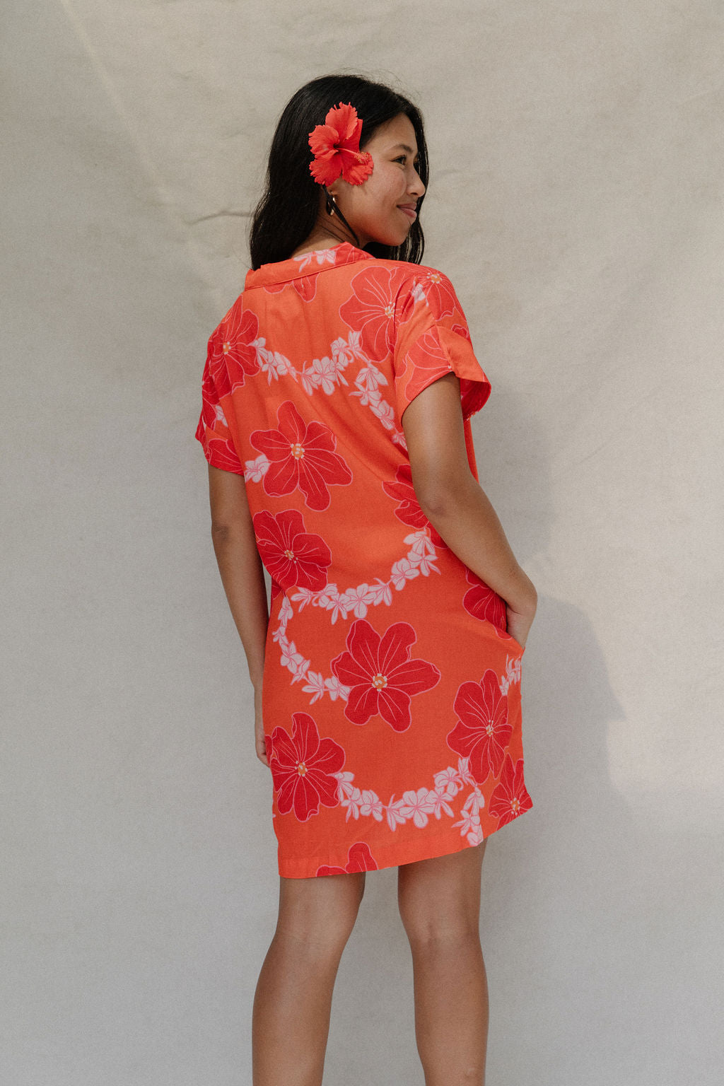 woman with brown hair wearing a retro orange v neck dress with flower pattern
