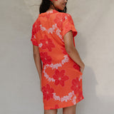 woman with brown hair wearing a retro orange v neck dress with flower pattern