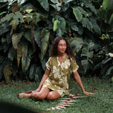 woman with brown hair wearing a shirt dress with v neck in green print with naupaka pattern