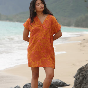 woman with brown hair wearing an orange v neck short sleeve dress with puakenikeni print