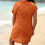 woman with brown hair wearing an orange v neck short sleeve dress with puakenikeni print