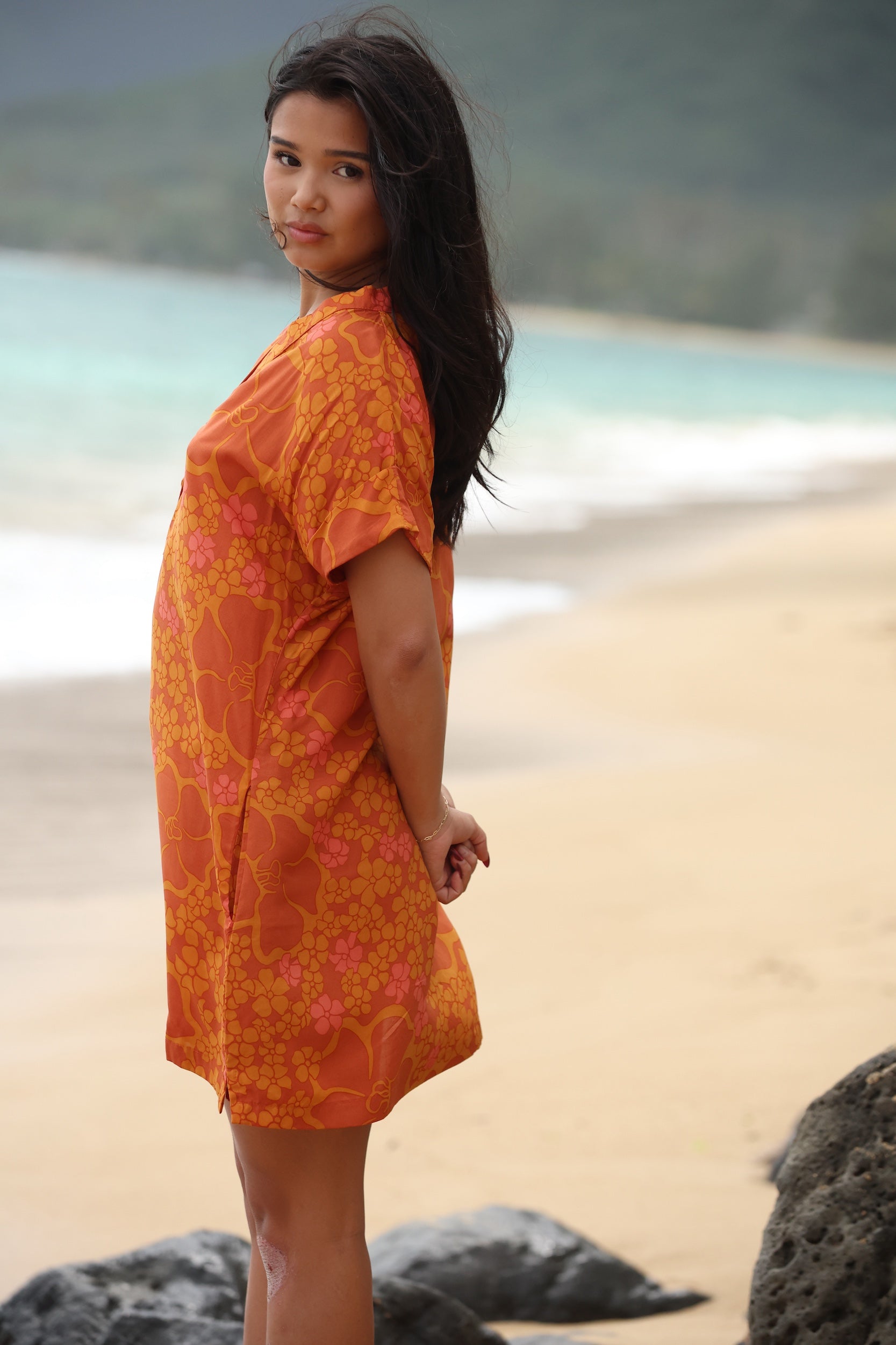 woman with brown hair wearing an orange v neck short sleeve dress with puakenikeni print