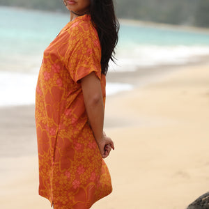 woman with brown hair wearing an orange v neck short sleeve dress with puakenikeni print