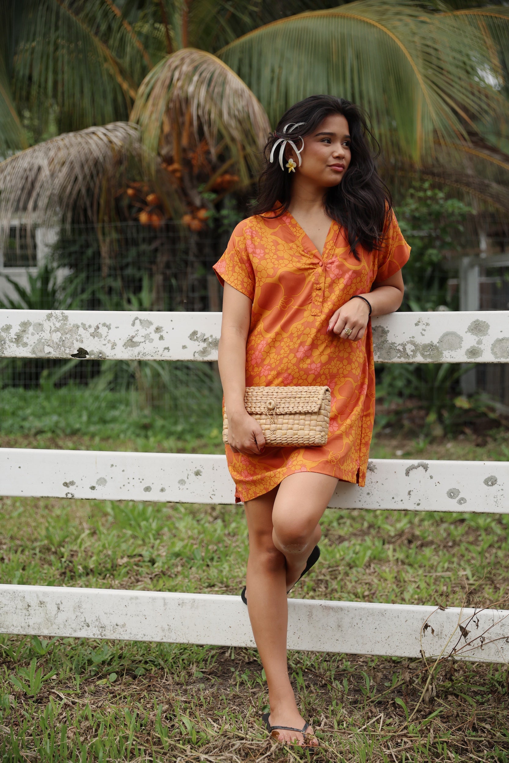 woman with brown hair wearing an orange v neck short sleeve dress with puakenikeni print