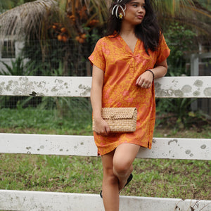 woman with brown hair wearing an orange v neck short sleeve dress with puakenikeni print