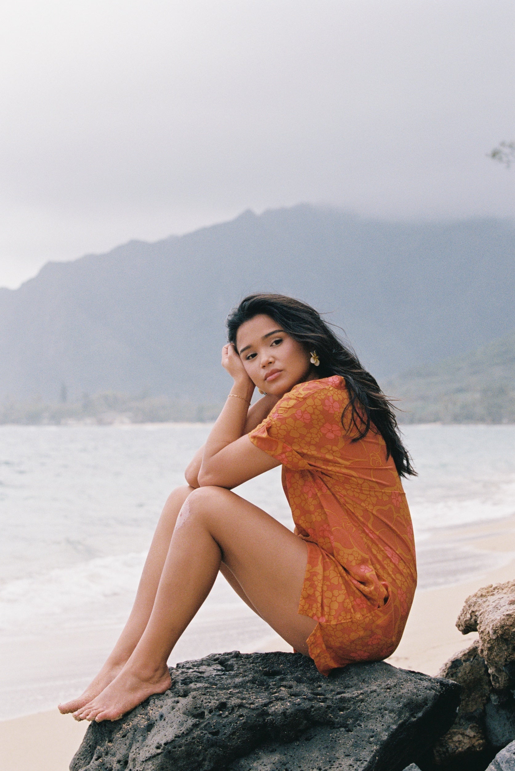 woman with brown hair wearing an orange v neck short sleeve dress with puakenikeni print