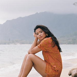 woman with brown hair wearing an orange v neck short sleeve dress with puakenikeni print
