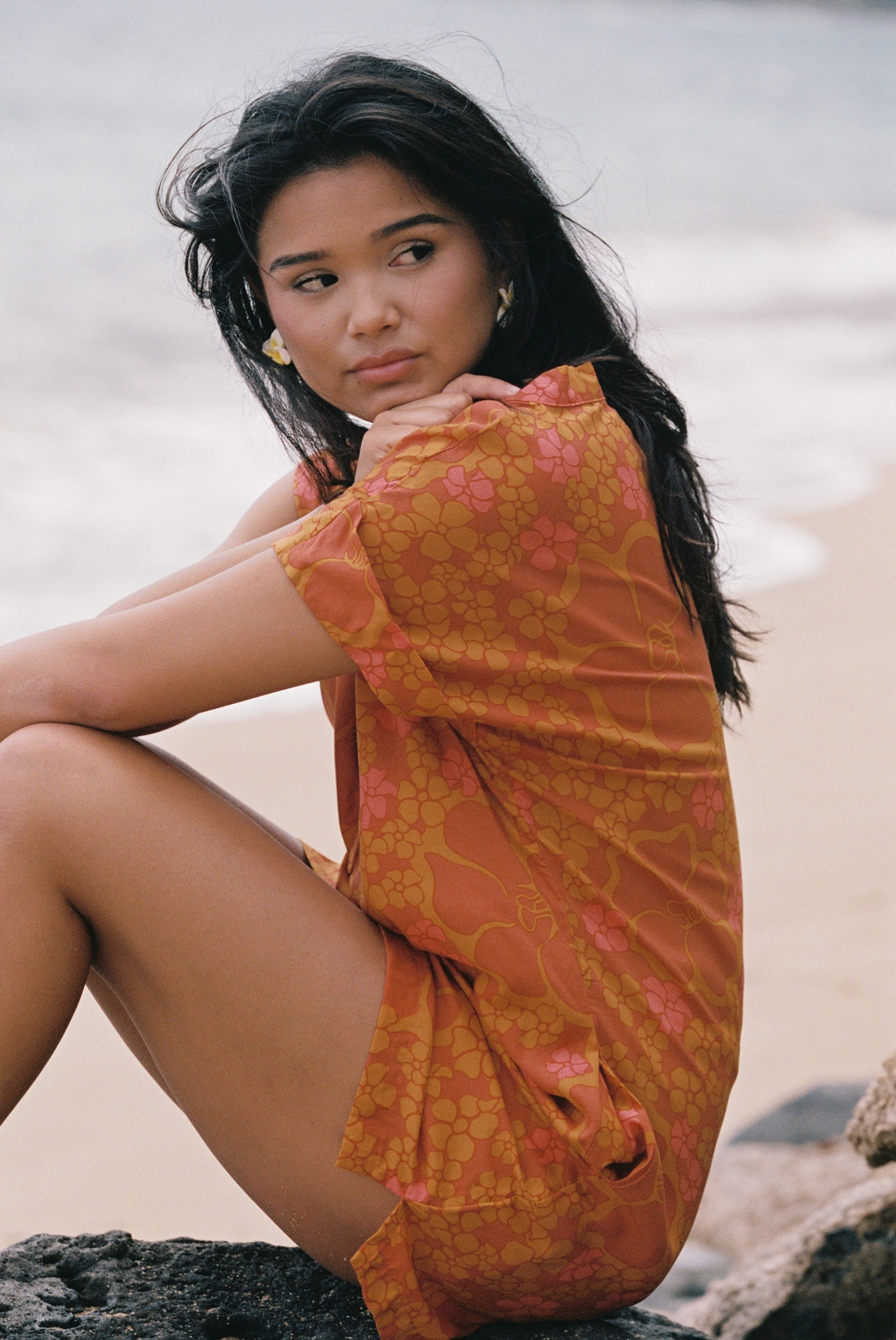 woman with brown hair wearing an orange v neck short sleeve dress with puakenikeni print