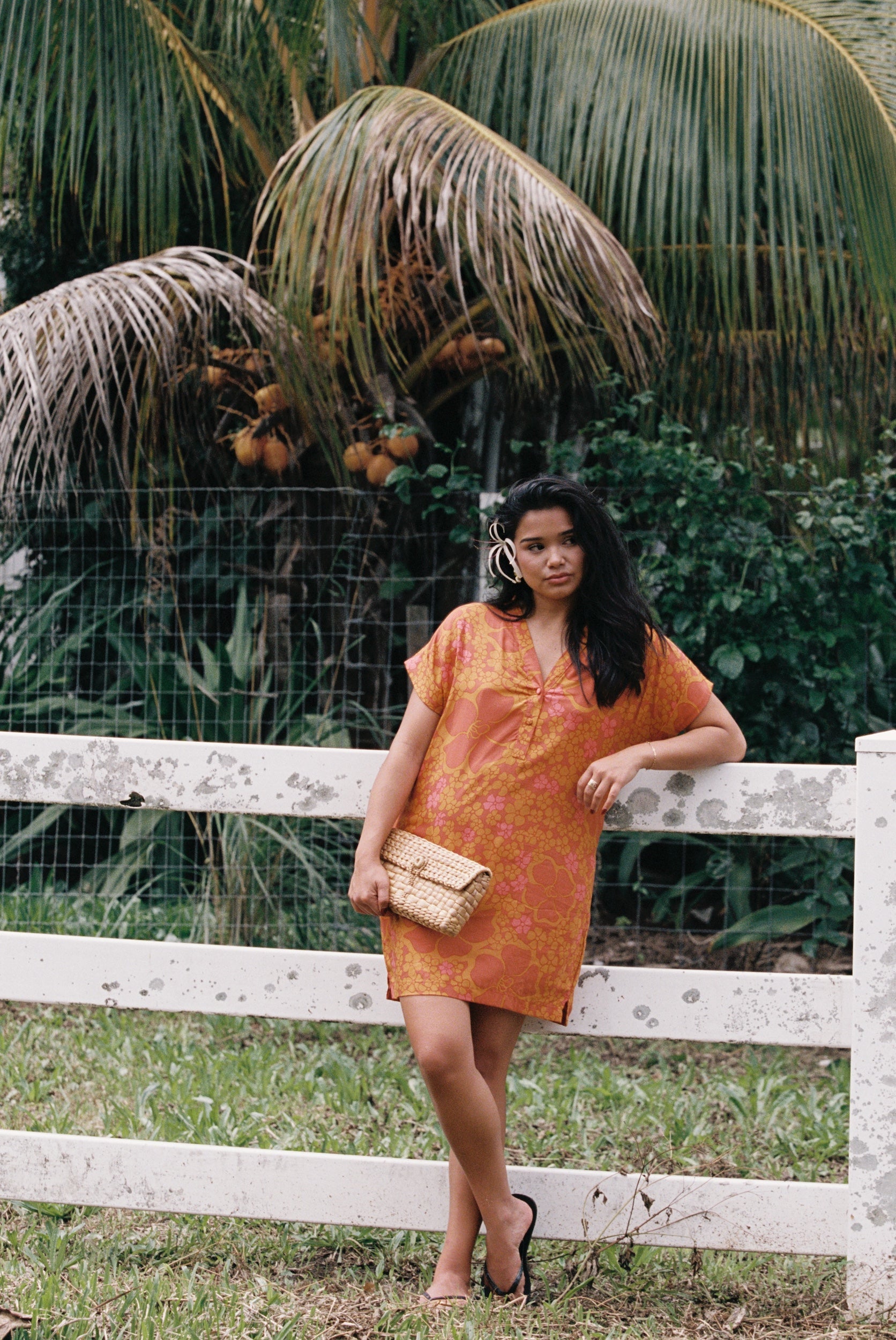 woman with brown hair wearing an orange v neck short sleeve dress with puakenikeni print