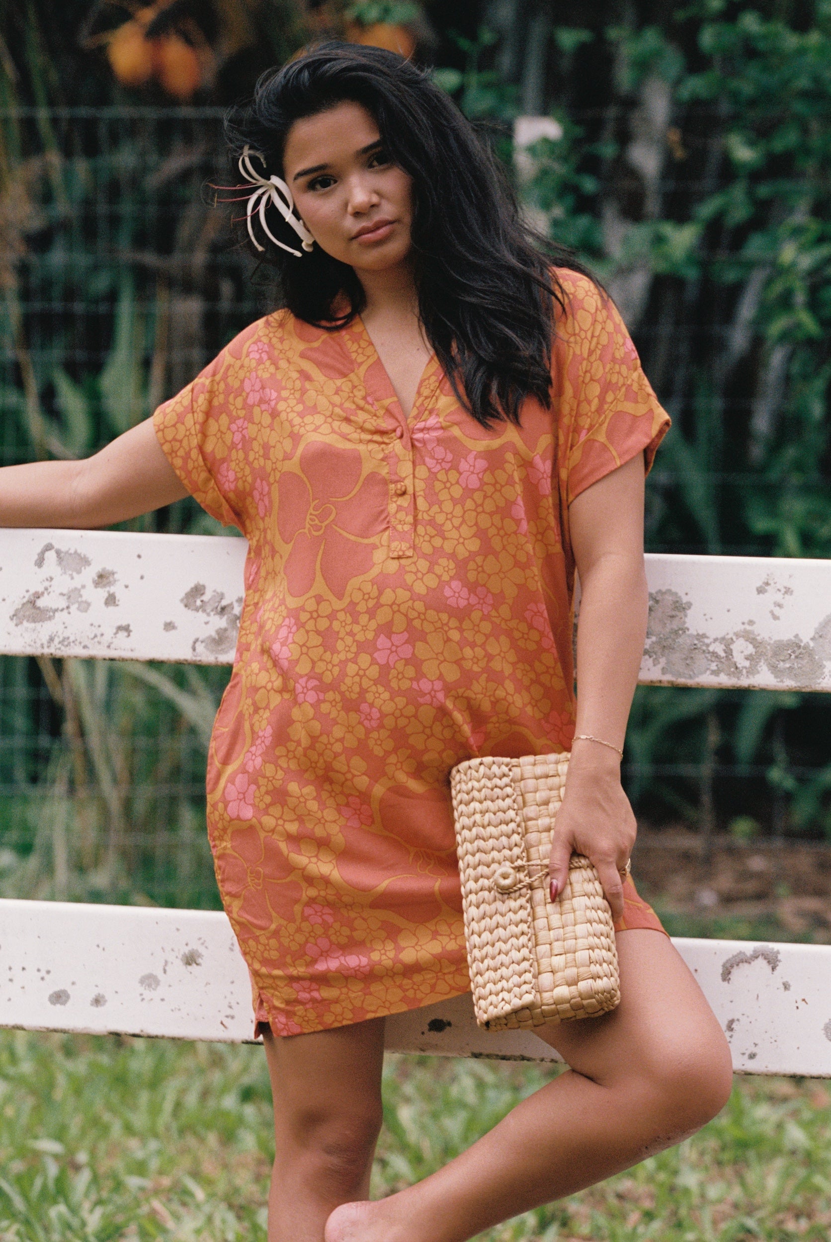 woman with brown hair wearing an orange v neck short sleeve dress with puakenikeni print