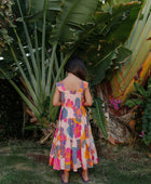 Girl wearing sleeveless long tiered dress with multi colored floral print on light pink ground.