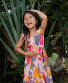 Girl wearing sleeveless long tiered dress with multi colored floral print on light pink ground.