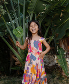 Girl wearing sleeveless long tiered dress with multi colored floral print on light pink ground.