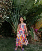 Girl wearing sleeveless long tiered dress with multi colored floral print on light pink ground.