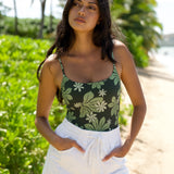 woman with brown hair wearing dark green active bodysuit with naupaka tiare print