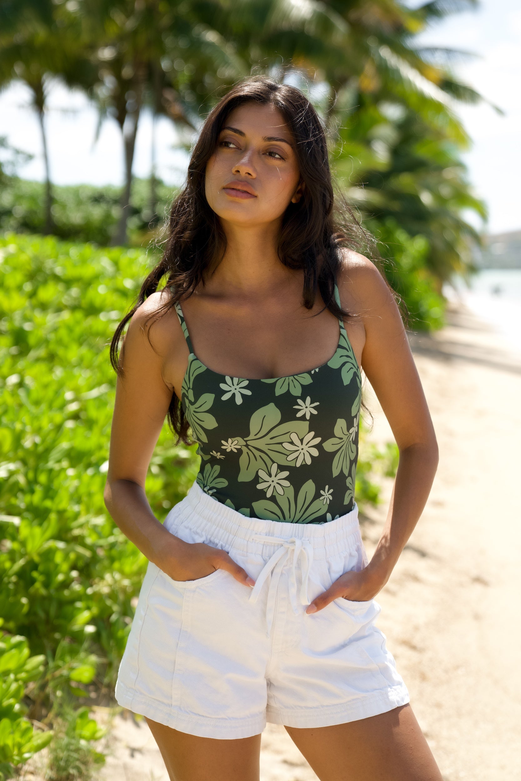 woman with brown hair wearing dark green active bodysuit with naupaka tiare print
