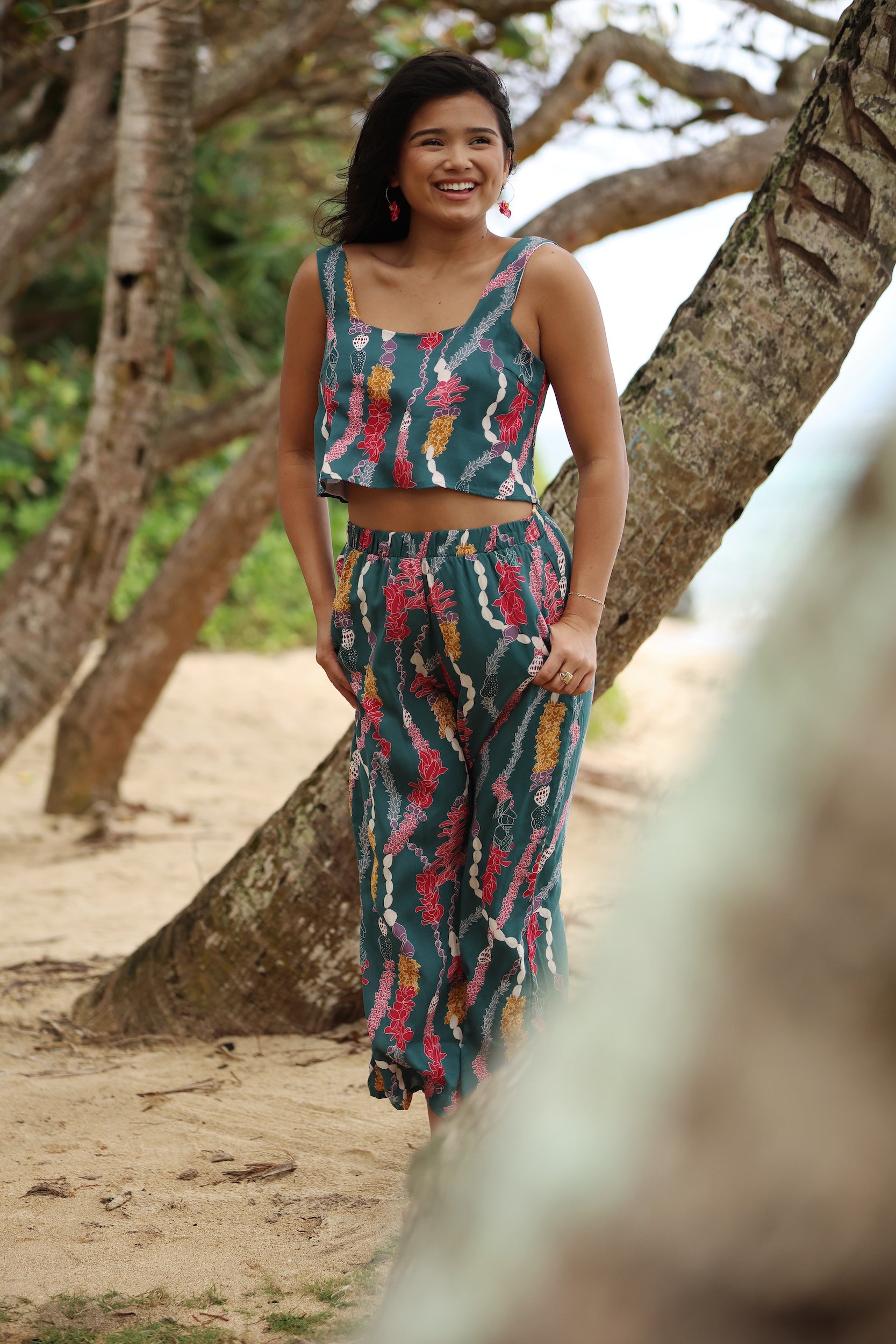 woman with brown hair wearing a matching top and pant set in dark teal with shell and lei print