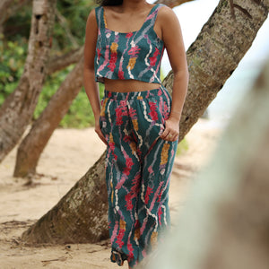 woman with brown hair wearing a matching top and pant set in dark teal with shell and lei print