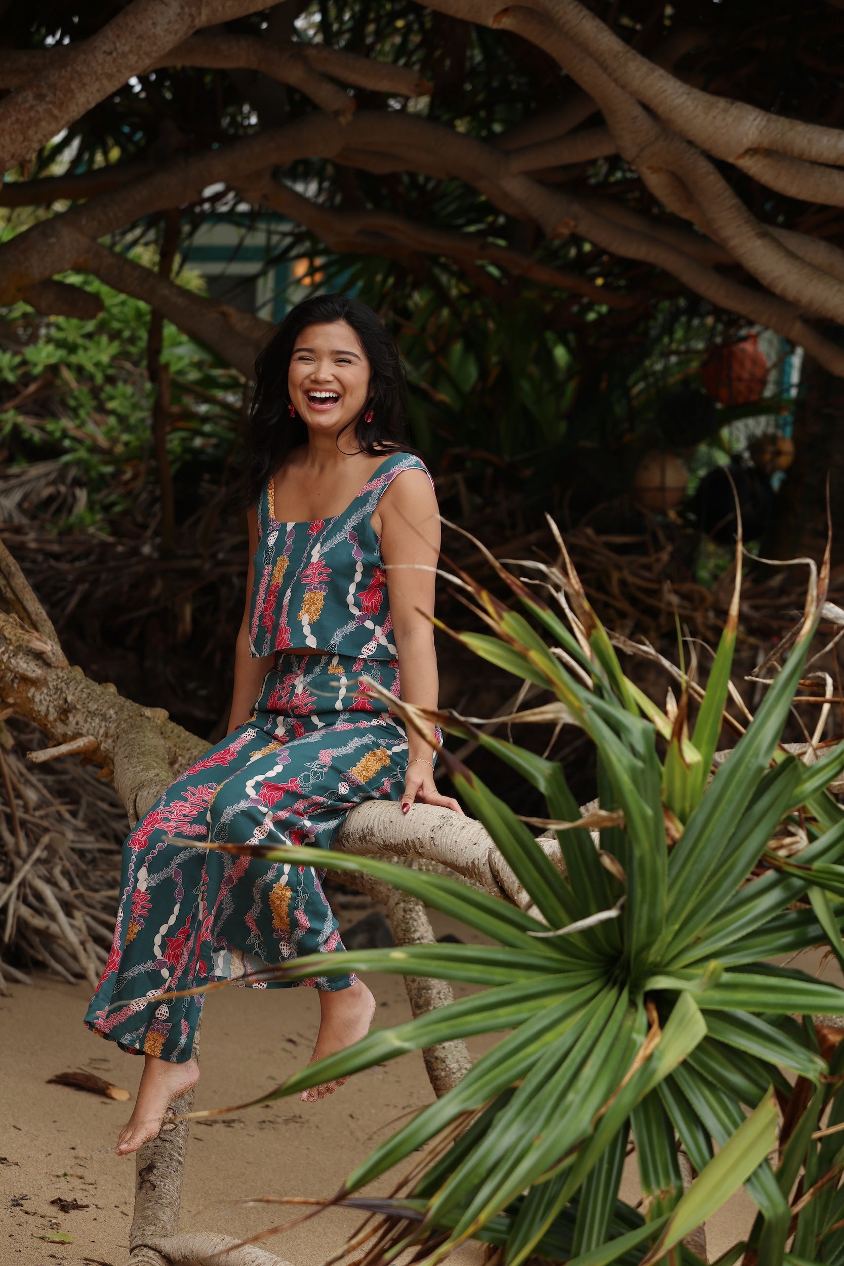 woman with brown hair wearing a matching top and pant set in dark teal with shell and lei print
