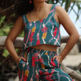 woman with brown hair wearing a matching top and pant set in dark teal with shell and lei print