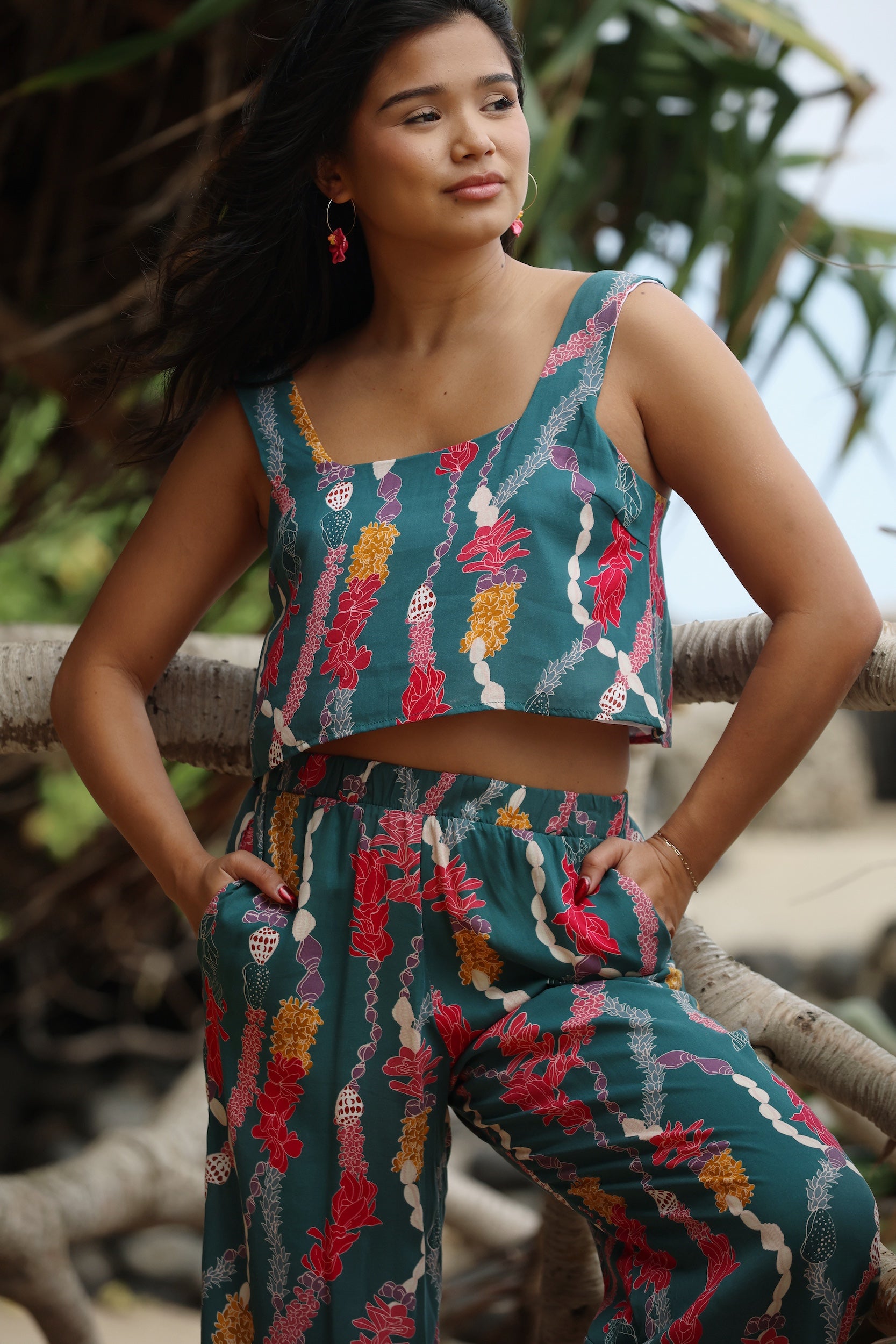 woman with brown hair wearing a matching top and pant set in dark teal with shell and lei print