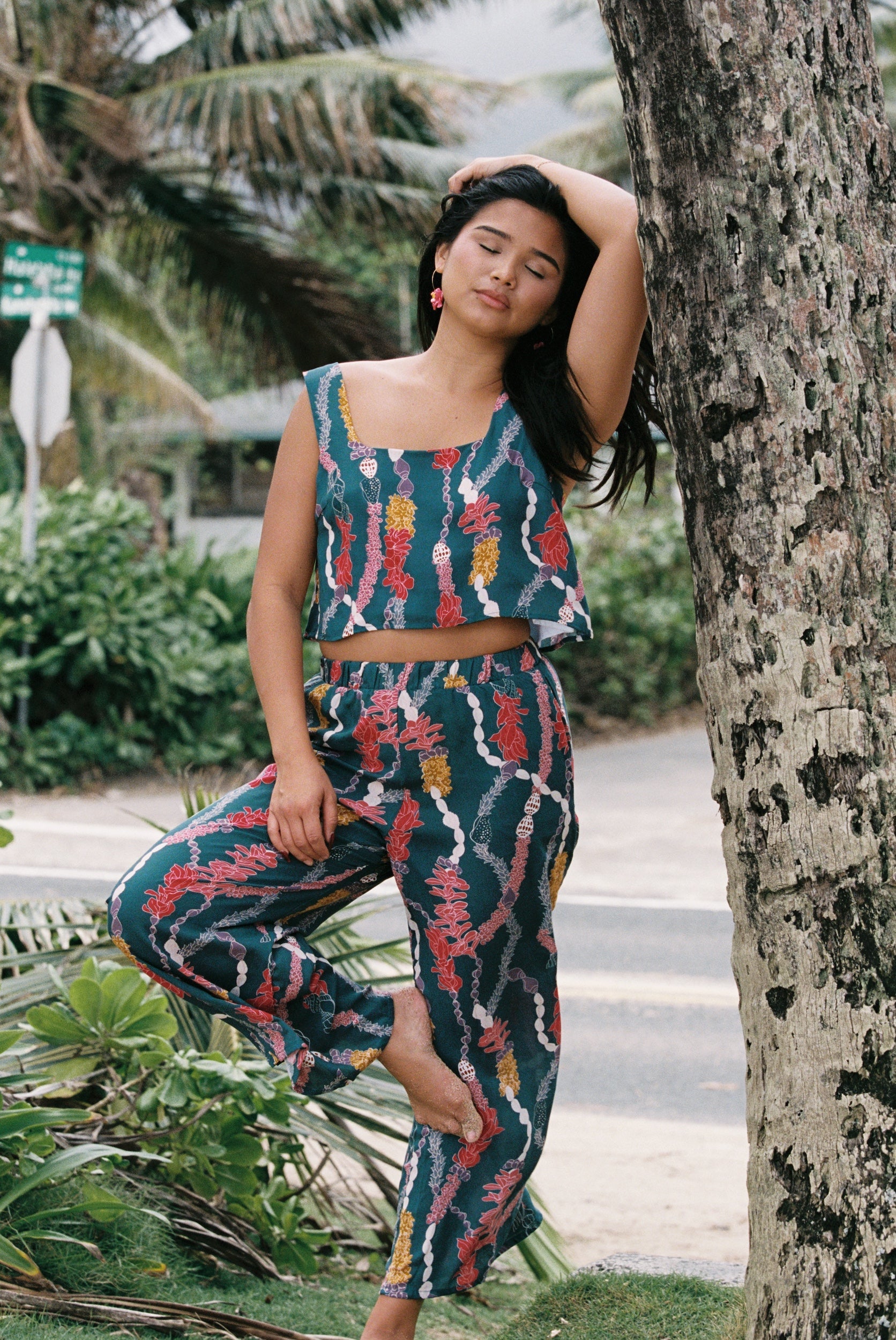 woman with brown hair wearing a matching top and pant set in dark teal with shell and lei print