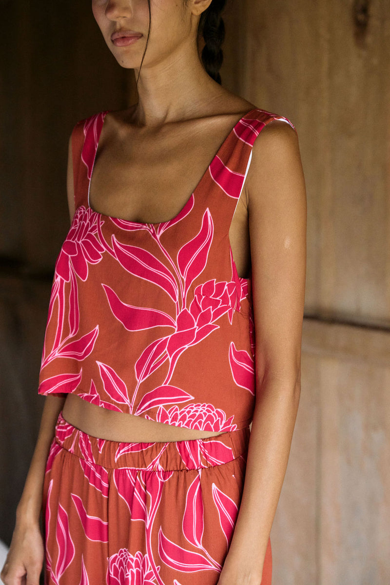 A woman with dark hair wears a YIREH flowy cropped top. It is the Naia Top in the Garden 'Awapuhi print. 