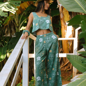 woman wearing lush green long flowy pants with puakenikeni