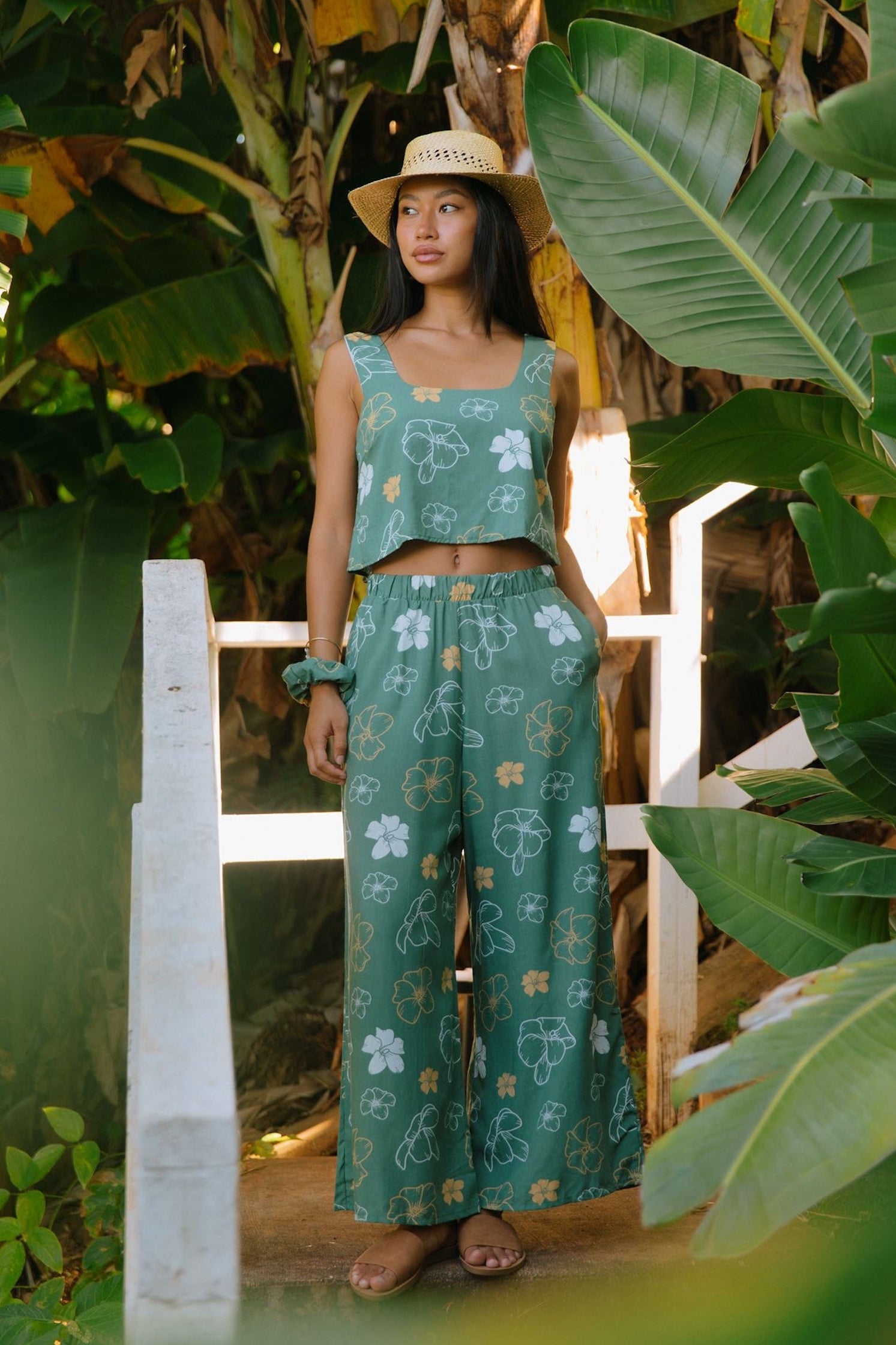 woman wearing lush green long flowy pants with puakenikeni