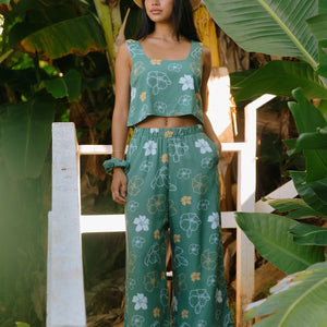 woman wearing lush green long flowy pants with puakenikeni