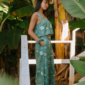 woman wearing lush green long flowy pants with puakenikeni