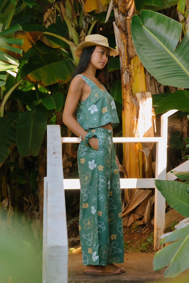 woman wearing lush green long flowy pants with puakenikeni