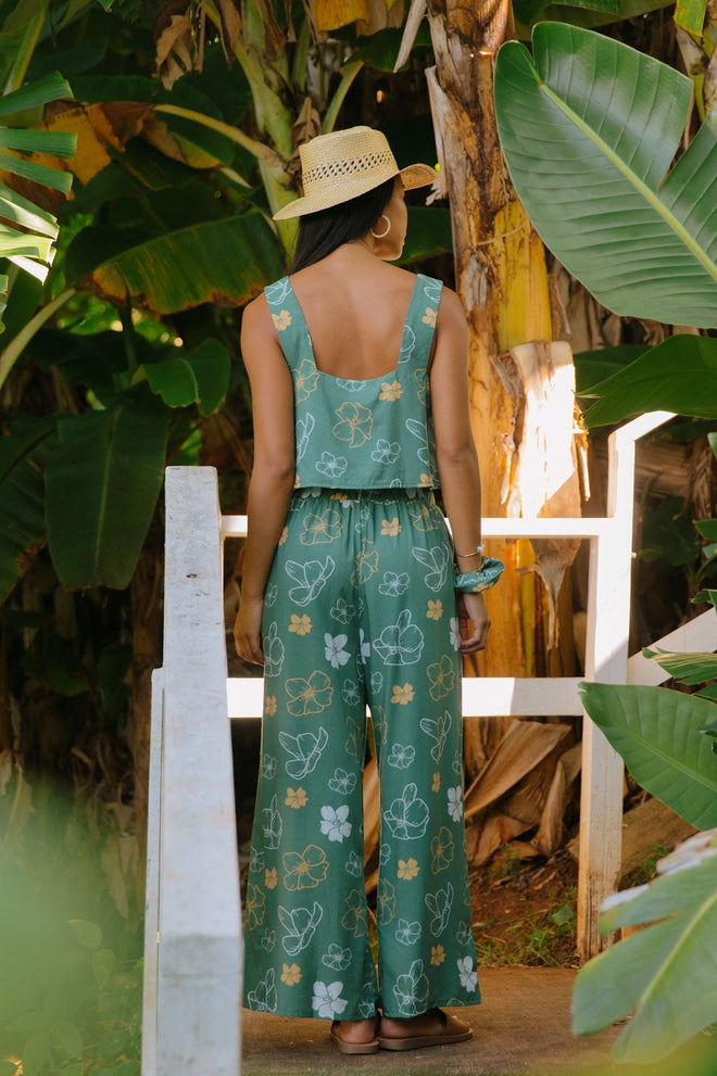 woman wearing lush green long flowy pants with puakenikeni