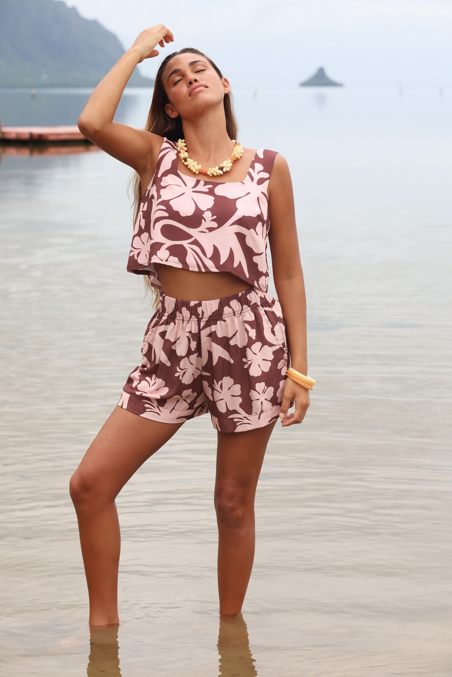 Woman with brown hair wearing a matching top and shorts set  in blush and brown hibiscus print. It is the Naia Top and Millie Shorts.