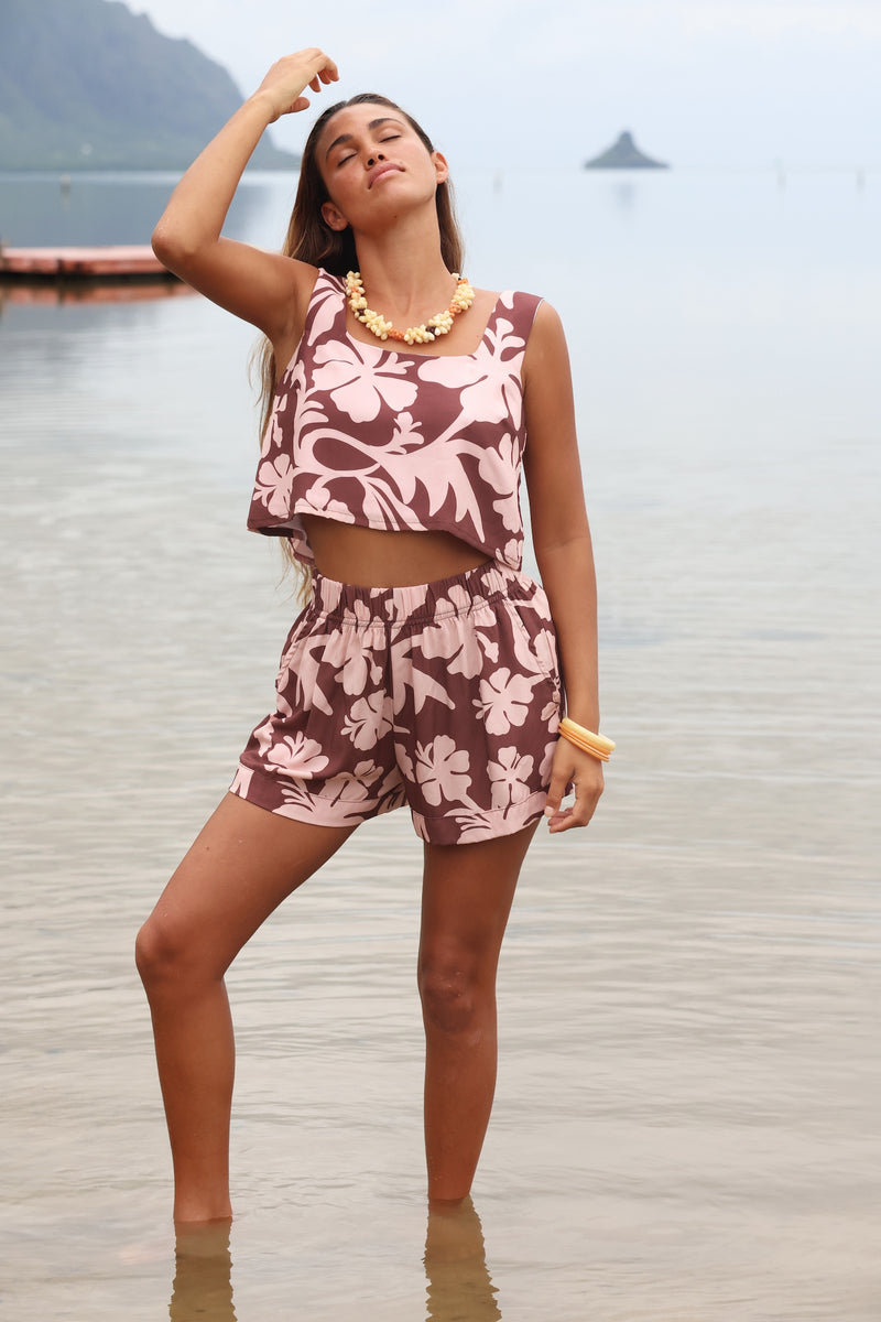 Woman with brown hair wearing a matching top and shorts set  in blush and brown hibiscus print. It is the Naia Top and Millie Shorts.