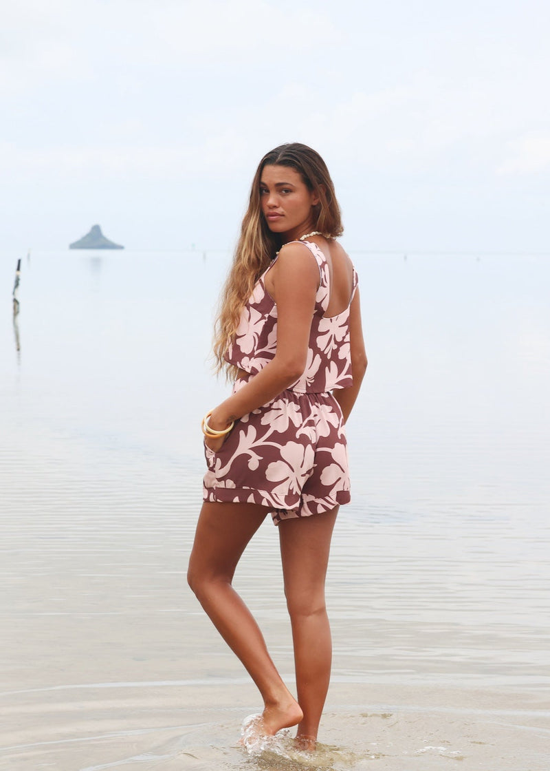 Woman with brown hair wearing a matching top and shorts set  in blush and brown hibiscus print. It is the Naia Top and Millie Shorts.