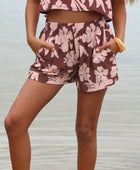 Woman with brown hair wearing a matching top and shorts set  in blush and brown hibiscus print. It is the Naia Top and Millie Shorts.